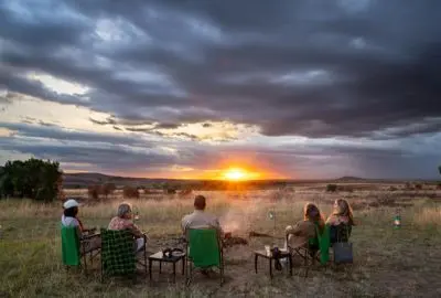 Guests gathered around a campfire as the sun sets over the Masai Mara