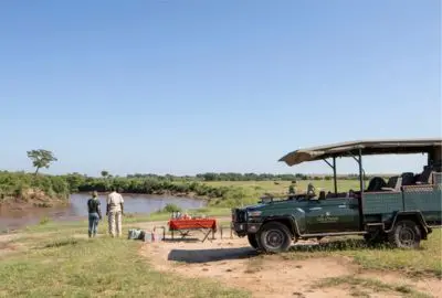 Safari vehicle and guests stopped beside a river in the Masai Mara