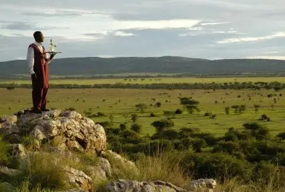 A lodge attendant carrying a tray on a rocky kopje above the Serengeti plains