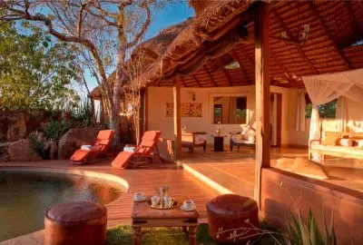 Open-fronted thatched cottage suite and sun loungers built into the kopje at Elsa’s Kopje
