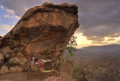 Sundowner table set beneath a giant balancing boulder at sunset