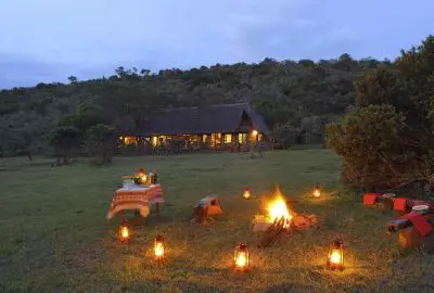 Lantern-lit bush dinner around a campfire outside a lodge at dusk