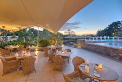 Terrace tables laid for dinner beside the pool at Hemingways Nairobi at dusk