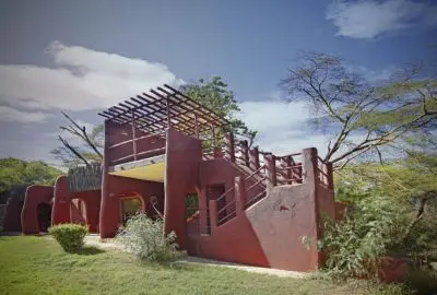 A red-walled lodge standing among acacia trees in Amboseli