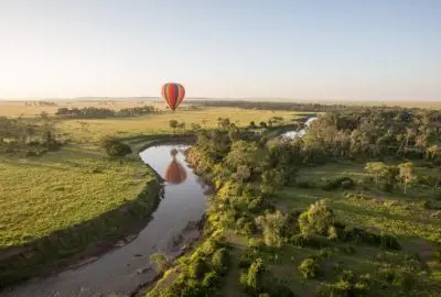 Hot air balloon drifting over the Mara River at sunrise