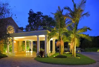 The colonnaded facade of Hemingways Nairobi lit up at night among tall palms