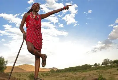 Maasai warrior in a red shuka pointing out across the plains