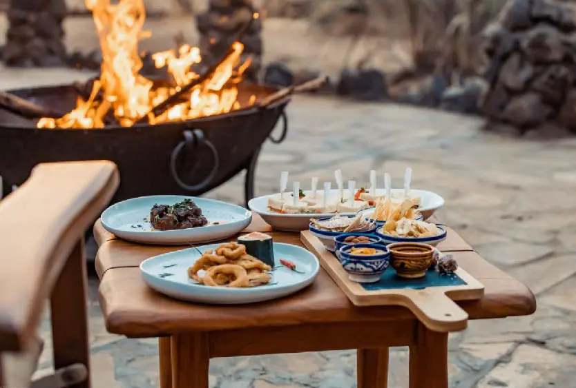 Dinner laid out on a wooden table beside a blazing fire pit at Soroi Amboseli