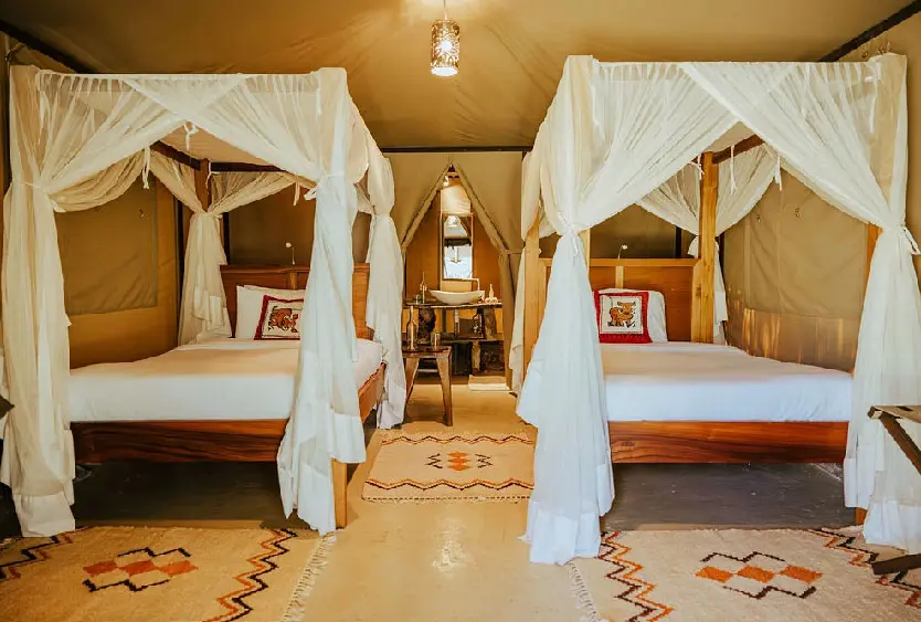 Twin beds draped in mosquito nets inside a tent at Soroi Luxury Migration Camp