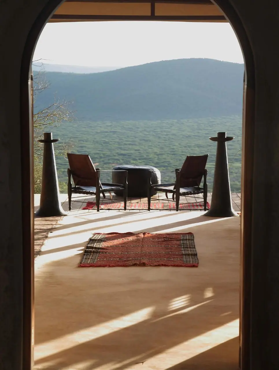 An arched lodge doorway opening onto a terrace with armchairs above green hills