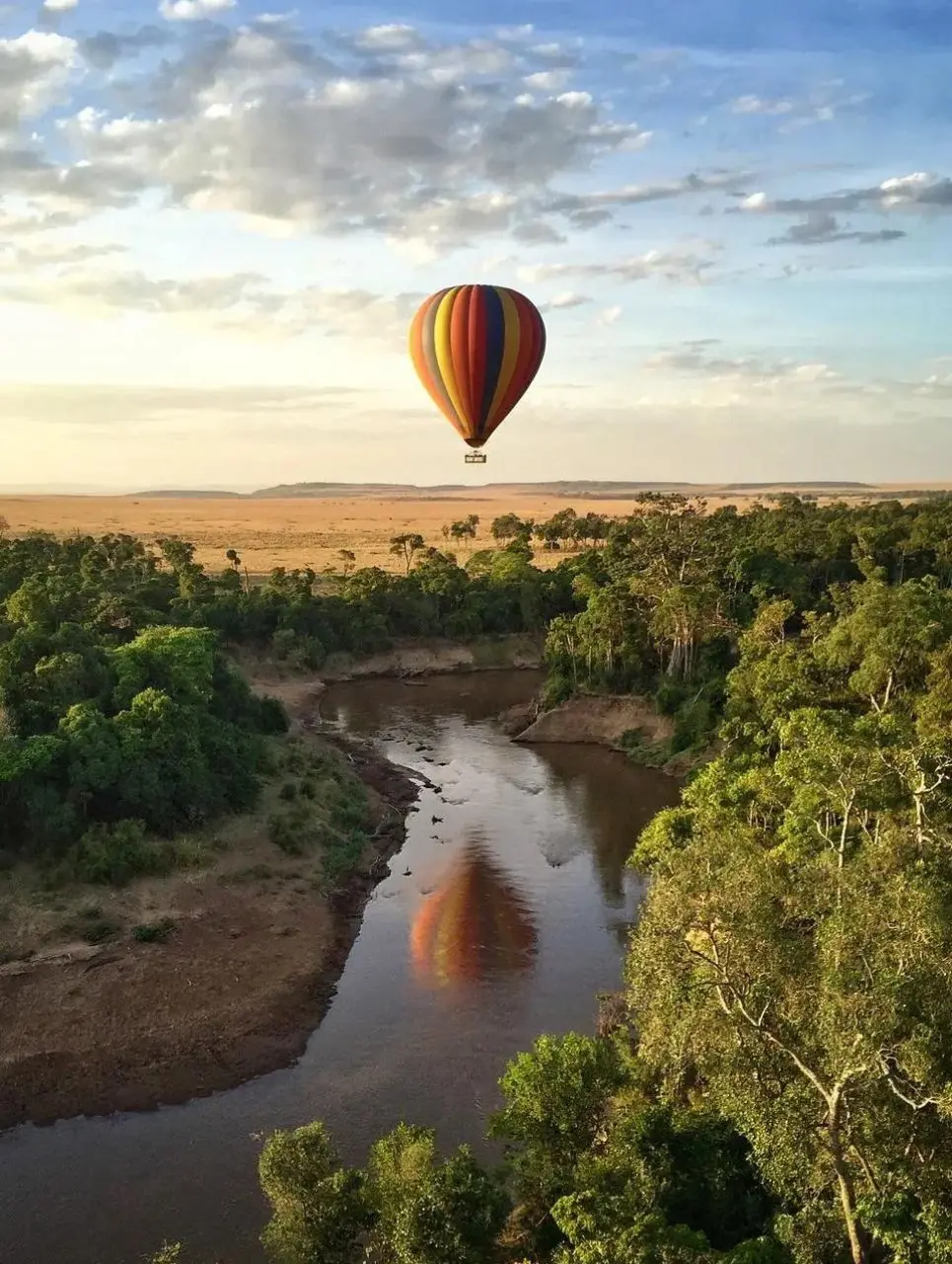 A hot-air balloon drifting at sunrise over the Mara river and open plains