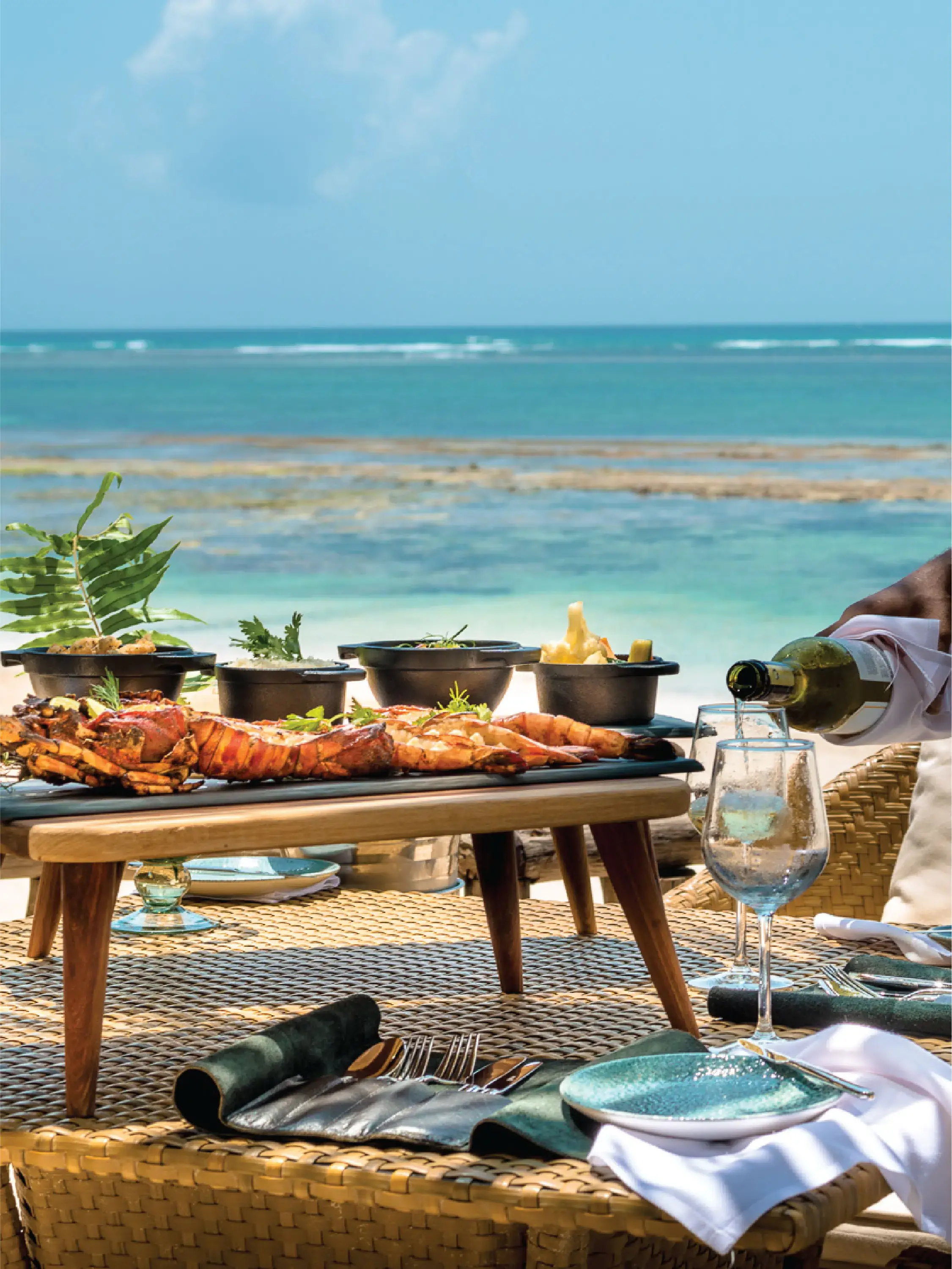 A seafood lunch laid on a beach table beside the turquoise Indian Ocean