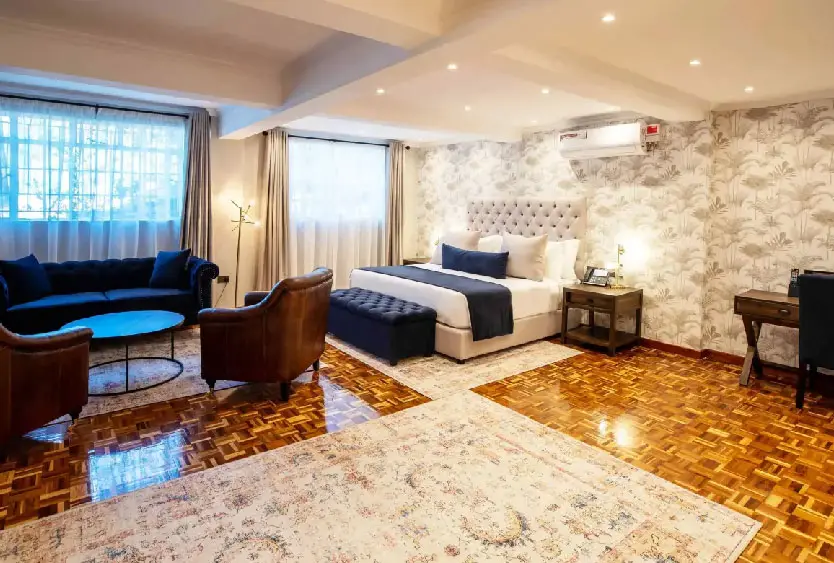Hotel bedroom with a wide upholstered bed, armchairs and warm parquet floor