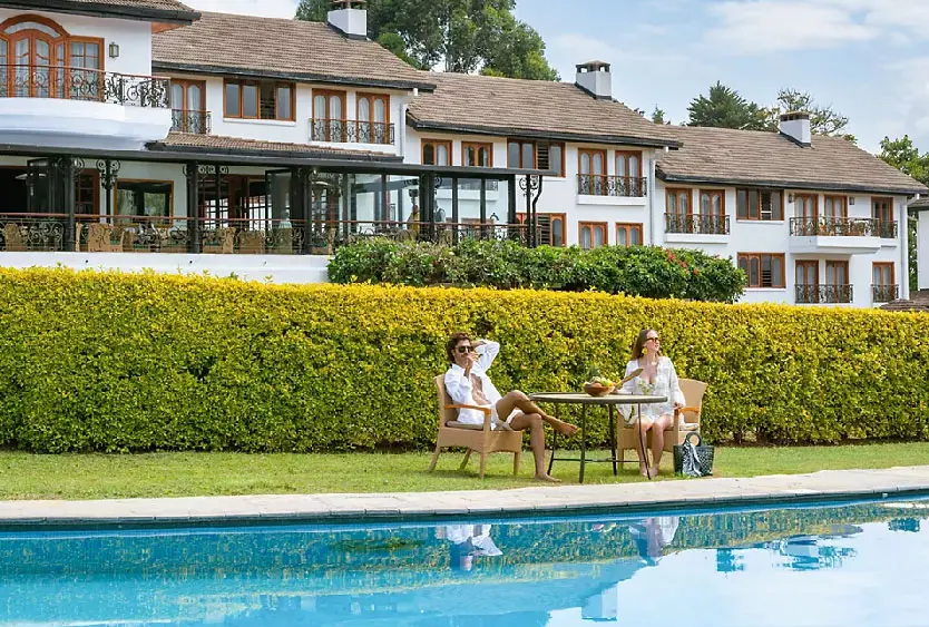 Two guests at a table on the lawn in front of the club’s white-gabled garden rooms