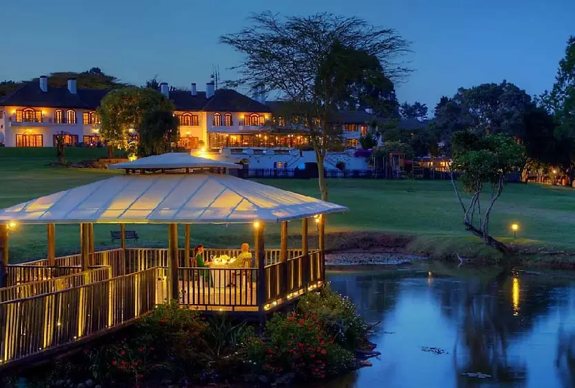 Lit lakeside deck and lodge buildings mirrored in still water at dusk
