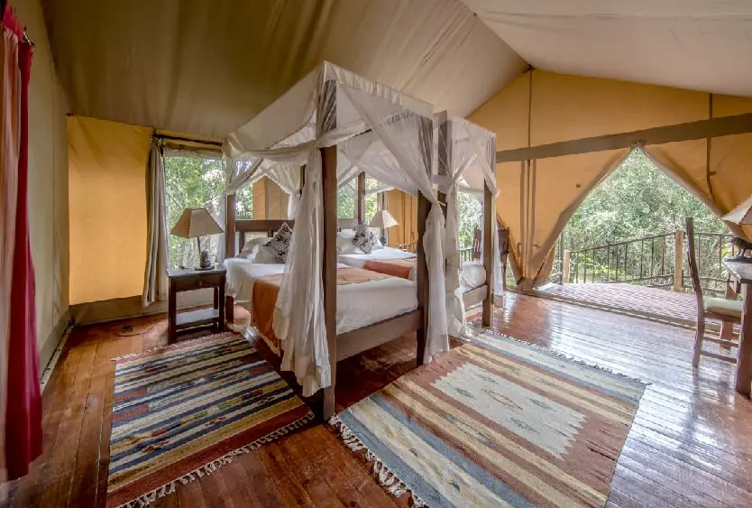 Canopied bed in a tented room opening onto a deck above the riverbank